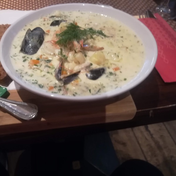 A bowl of creamy seafood soup with mussels and dill, brown bread alongside