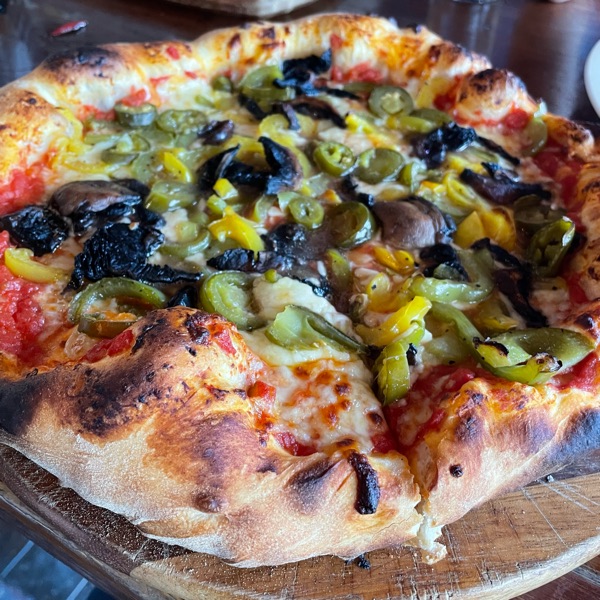 A stone-baked pizza with a blistered crust, peppers, jalapeños and mushrooms
