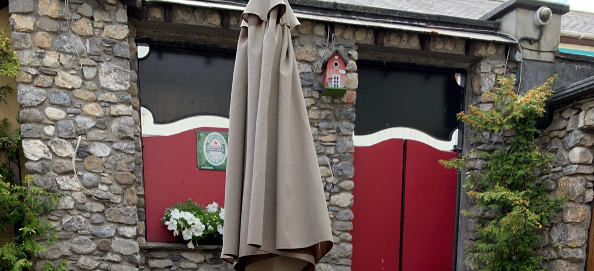 The beer garden: rubble-stone walls, red doors with white scalloped trim, planters and a furled parasol