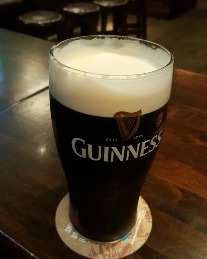 A freshly settled pint of Guinness on a dark wooden table, bar stools behind
